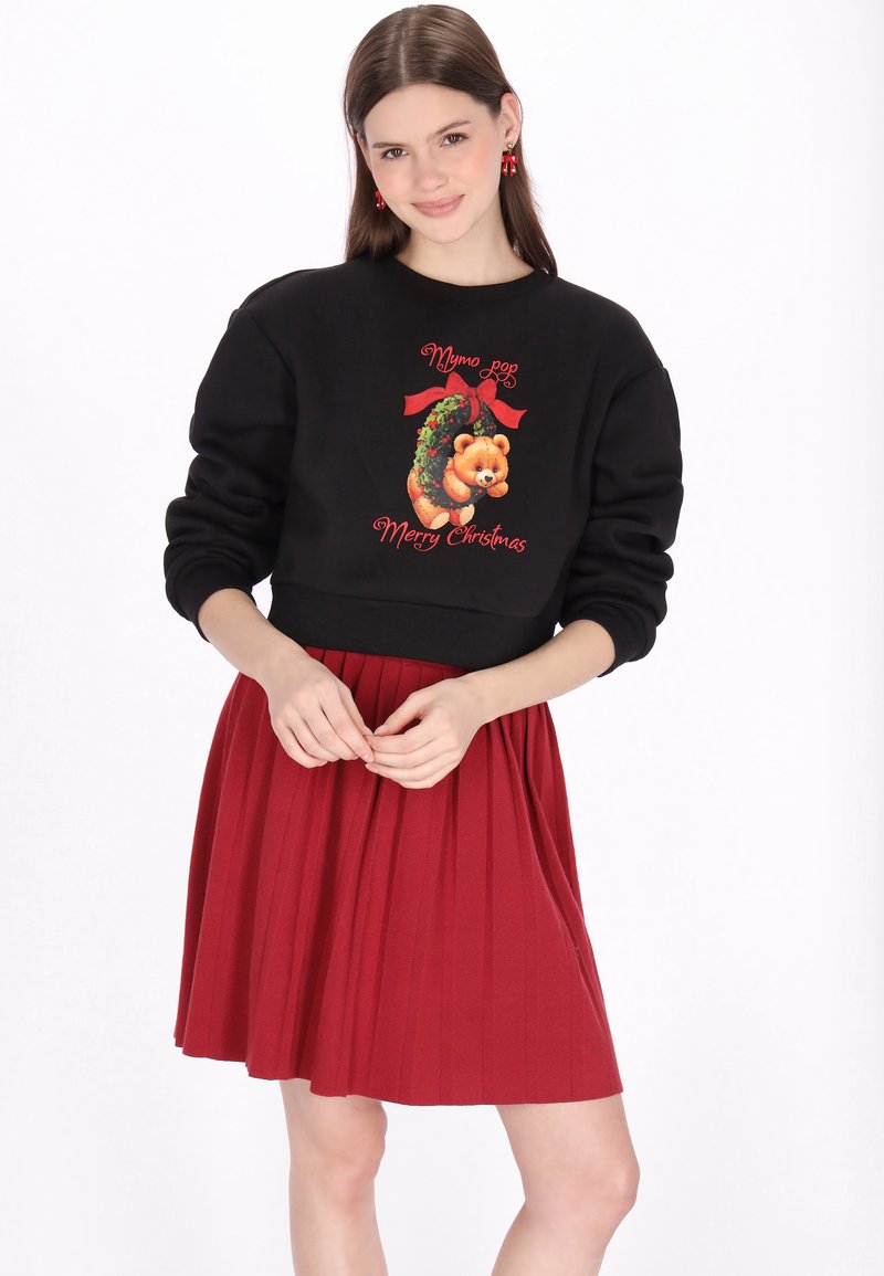 Sudadera negra con un estampado festivo de oso, detalles en rojo y texto "Feliz Navidad", combinada con una falda plisada roja.