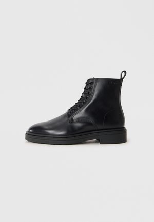 Black leather lace-up ankle boot with pull tab and flat sole, shown from the outer side on a plain white background.