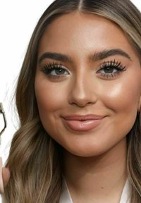 Récourbe-cils en métal tenu dans une main, avec une finition argentée brillante. Le modèle a de longs cheveux châtain clair et une peau lisse avec un maquillage naturel.