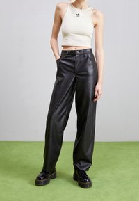 Vitt ribbat crop top med svart logga, parat med högmidjade svarta faux läderbyxor med vida ben och kraftiga svarta snörkängor.