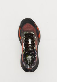 Baskets noires et rouges avec une tige texturée présentant un motif floral, des lacets noirs, une semelle rembourrée et un logo sur la languette.