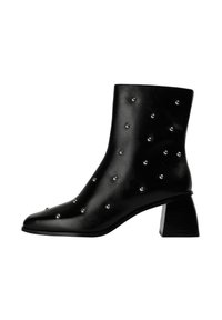 Bota tobillo de cuero negro con punta puntiaguda, decorada con tachuelas plateadas y un tacón grueso de bloque. Textura suave y diseño elegante.