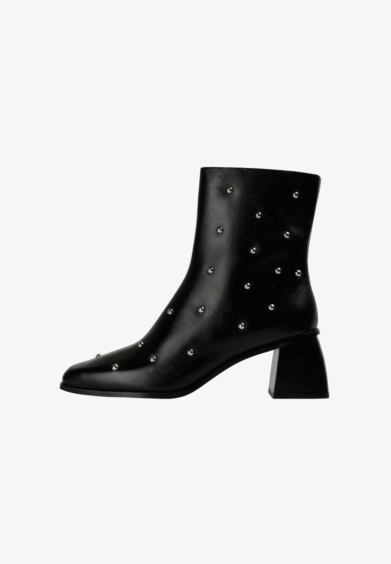 Bota tobillo de cuero negro con punta puntiaguda, decorada con tachuelas plateadas y un tacón grueso de bloque. Textura suave y diseño elegante.