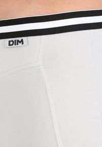 Pánske svetlošedé boxerky s čierno-bielym pruhovaným pásom. Vyznačujú sa mäkkou, elastickou látkou a šitými švami. Viditeľné logo DIM.