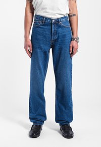 Vaqueros de mezclilla azul con un ajuste ligeramente holgado, cintura alta y diseño de cinco bolsillos. La tela tiene una textura suave y un desgaste mínimo.