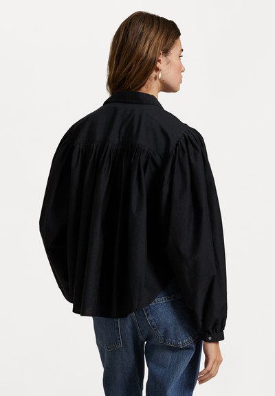 Svart puffermet skjorte i bomull med samlet bak, funksjoner krage og knappedeler, kombinert med blå denimjeans.