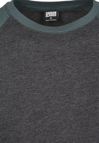 Ciemnoszara koszulka z okrągłym dekoltem i zielonymi akcentami na kołnierzu. Wykonana z miękkiej tkaniny, o gładkiej, równomiernej fakturze.