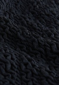 Gros plan d'un tissu tricoté noir avec des motifs torsadés détaillés et des brins de fil texturés et entrelacés.