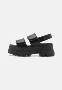 Black platform sandals featuring two wide straps with Velcro closures. Chunky rubber sole with ridged traction pattern and open back design.
