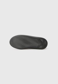 Black shoe sole with wavy textured tread and a large "K" shape near the heel on a plain white background.