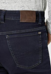 Marineblauwe spijkerbroek met een rechte pijp, voorzien van contrasterende stiksels, een bruin leren label op de tailleband en minimalistische pocketdetails.