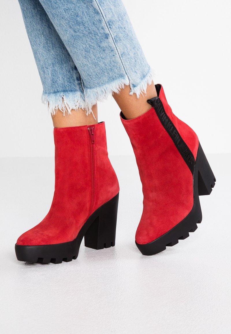 Botines de ante rojos con tacones gruesos negros y suelas de goma con buen agarre, llevados con jeans claros desgastados.