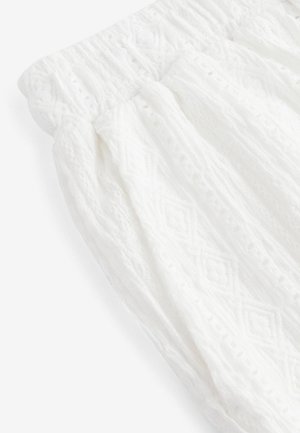 Vitt strukturerat tyg med ett diamantsmönster. Elastisk midja med rynkdetaljer. Lätt och luftigt material som passar för varma väderförhållanden.