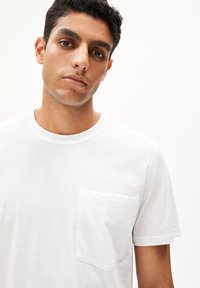 Weißes Baumwoll-T-Shirt mit Rundhalsausschnitt und kurzen Ärmeln. Verfügt über eine Brusttasche und eine glatte, leichte Textur.