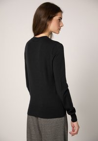 Maglione nero lavorato a maglia con collo rotondo, vestibilità aderente e maniche lunghe, caratterizzato da polsini e orlo a coste. Tessuto strutturato con finitura liscia.