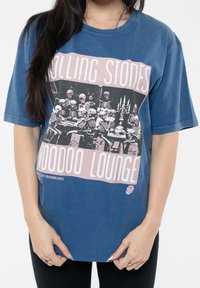 Blue cotton t-shirt featuring a graphic print of skeletons at a table, with "Rolling Stones Voodoo Lounge" text in pink and white.