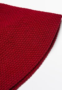 Red knitted textile with a textured, woven pattern. The edges are rolled, showcasing the thick yarn and a warm, cozy appearance.