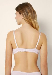 Vaaleanpunainen rintaliivi, jossa on säädettävät olkaimet ja pitsireunus takaosa, varustettu hakaset ja silmukat -kiinnityksellä. Silkkinen kangas.