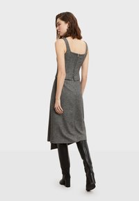 Haljina od sivog vune s dizajnom bez rukava i kvadratnim dekolteom, koja ima zip zatvaranje na leđima i lepršavu suknju. Uključene crne čizme do koljena.