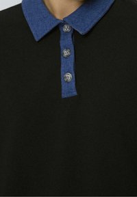 Polo noir avec un col en denim, comportant quatre boutons. Texture lisse avec des couleurs contrastantes bleu et noir.