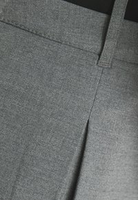 Pantaloni grigi realizzati in tessuto testurizzato, con una piega frontale e una vita liscia. La vista ravvicinata mostra la cucitura dettagliata e la trama.