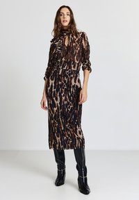 Abito midi con stampa animalier, caratterizzato da tessuto trasparente, colletto con rouches e maniche lunghe. Indossato con stivali neri al ginocchio, creando una silhouette elegante.