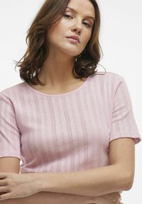 Top rosa chiaro con maniche corte, caratterizzato da un motivo testurizzato di linee verticali e piccoli design a zigzag, scollatura rotonda e forma aderente.
