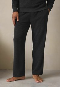 Mørkegrå loungedragter lavet af blødt, tekstureret stof, med en afslappet pasform, sidelommer og en let afsmalnet nederste kant.
