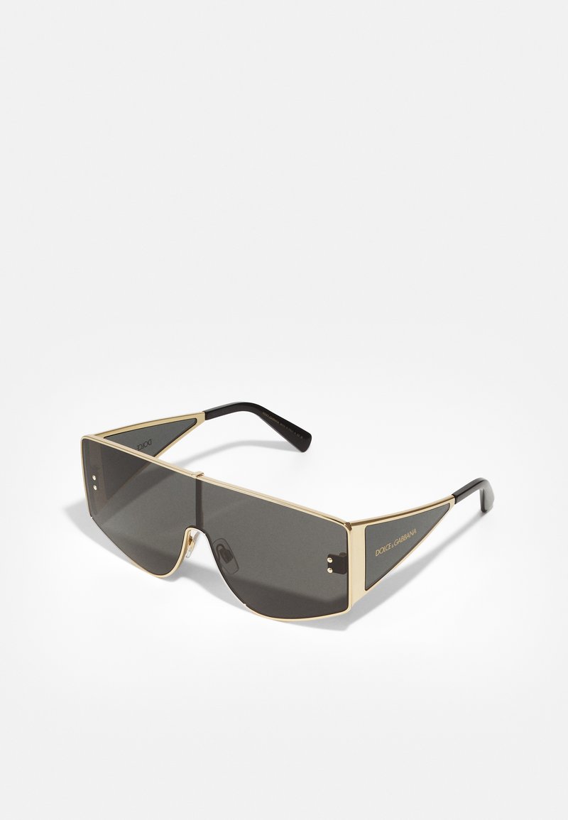Sunglasses with black tinted lenses, bold gold metal frame, angular design, and black accents on temples. Unique shape and detailing.