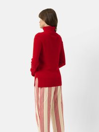 Rode coltrui met een geribbelde textuur, voorzien van zijsplitten. Gecombineerd met crèmekleurige broek met verticale rode strepen.