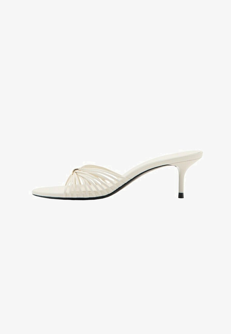 Beige open-toe mule sandaal met naaldhak en dunne, gebogen bandjes over de voorkant.