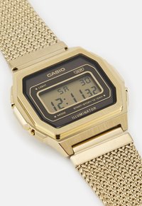 Guld digital klocka med rektangulärt urtavla, svart display, nätmetallarmband och olika funktionsknappar. Har märket "Illuminator".