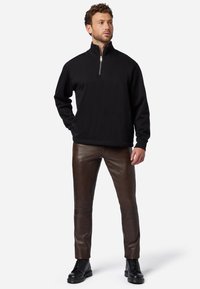 Zwarte zip-up pullover van zachte stof, gecombineerd met strakke donkerbruine leren broeken en zwarte veterschoenen. Eenvoudige, moderne silhouet.