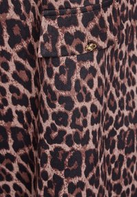 Tessuto a motivo leopardato caratterizzato da una miscela di marrone e nero, con una superficie testurizzata e un piccolo accento dorato su una tasca.