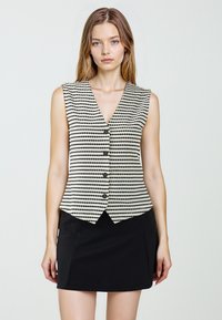 Mouwloos vest met een V-hals, gekenmerkt door zwart-witte streeppatronen, zes zwarte knopen en een getailleerd ontwerp, gecombineerd met een zwarte rok.