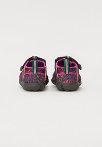 Dwa buty w kolorze ciemnopurpurowym z jaskrawo-różowymi i czerwonymi abstrakcyjnymi wzorami. Wśród cech znajdują się zielone paski do ciągnięcia oraz solidna czarna podeszwa.