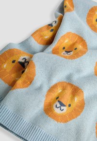 Manta de punto de color azul claro con patrones de caras de león naranja, con un borde acanalado. Textura suave, diseño juguetón y colores vivos.