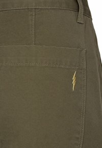 Olive green pants with a textured fabric, featuring a back pocket and a small golden lightning bolt embroidery detail.