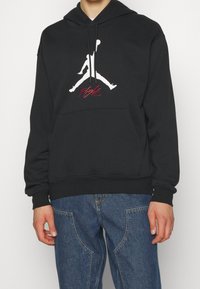 Felpa nera con cappuccio realizzata in misto cotone, con un grande logo Jumpman bianco e testo rosso "Flight". Tasche frontali a marsupio e cappuccio regolabile con cordino.