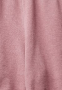 Tissu tricoté rose doux avec une texture fine et un pli vertical subtil créant des ombres douces.