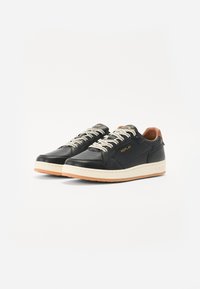 Sneakers negre din piele cu detalii perforate, talpă din cauciuc bej, șireturi crem și accent de toc din piele maro. Logo-ul brandului este afișat.