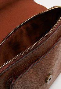 Brązowa torba skórzana o teksturowanej powierzchni z otwartym złotym zamkiem, ukazującym miękkie brązowe wnętrze z tkaniny oraz zapięciem na magnes.