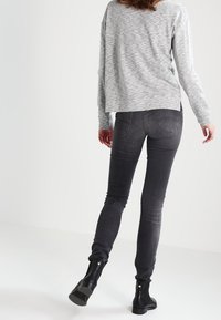 Maglia grigia a maniche lunghe con vestibilità ampia, abbinata a jeans skinny blu scuro e stivali neri alla caviglia. Texture morbide, design semplice.