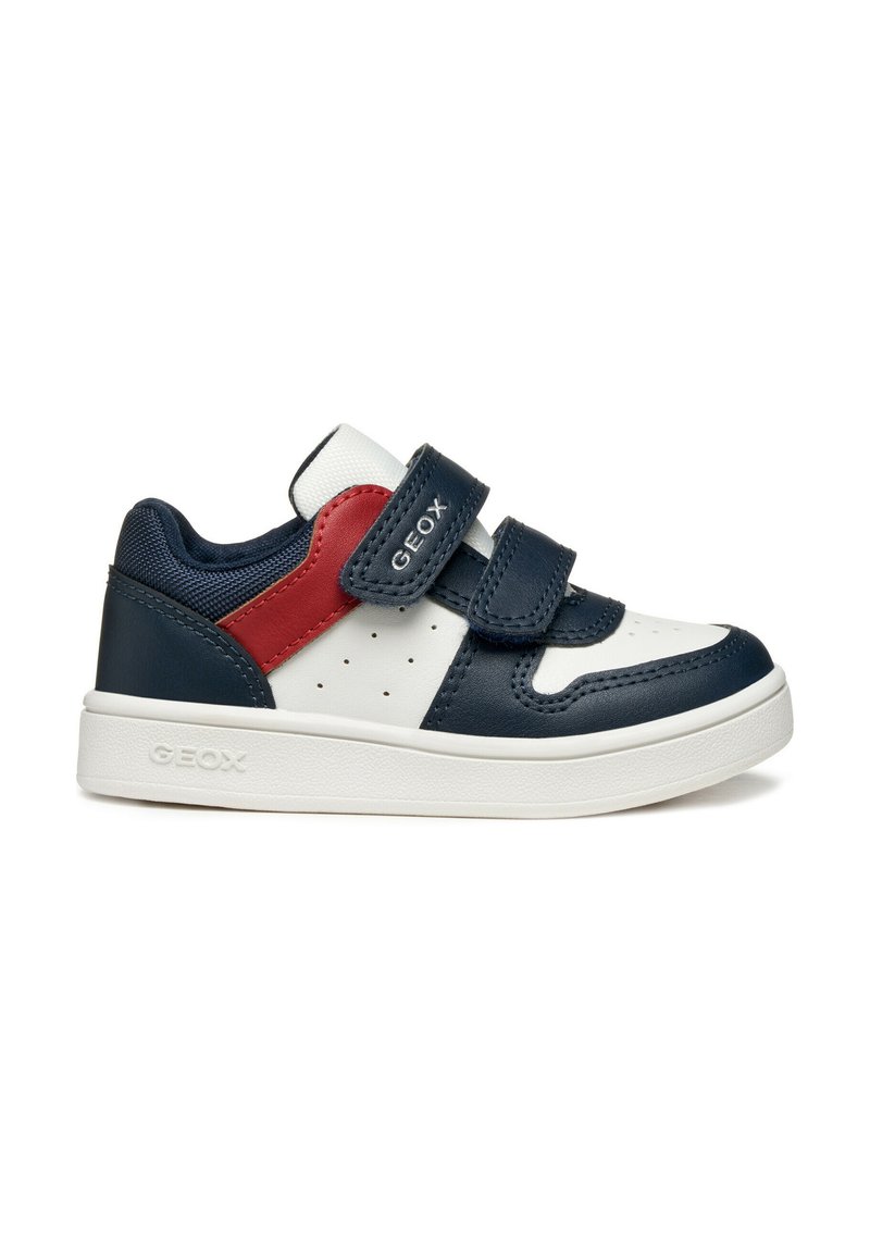 Baskets en cuir bleu marine et blanc avec des accents rouges, des bandes Velcro, des côtés perforés et une semelle en caoutchouc blanc texturé. Nom de la marque visible.