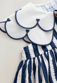 Gestreiftes Kleid in Blau und Weiß mit einem gewellten Kragen mit marinefarbener Umrandung und Herzmotiven. Strukturierter Stoff mit gerafftem Rockdesign.