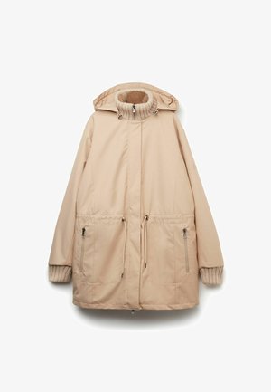 Beżowa wodoodporna parka z wysokim kołnierzem, regulowaną talią na sznurki, kieszeniami zapinanymi na zamek oraz ściągaczami przy mankietach. Gładka tekstura i kaptur.