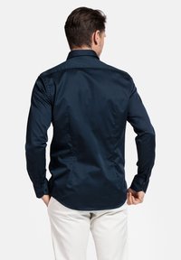 Navyblauw overhemd met lange mouwen, een puntige kraag en knoopmanchetten, met een gladde, matte textuur en een getailleerde pasvorm.