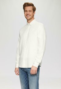 Chemise blanche à manches longues en tissu doux avec un col et une texture subtile, associée à un jean bleu clair.