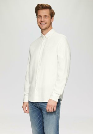 Chemise blanche à manches longues en tissu doux avec un col et une texture subtile, associée à un jean bleu clair.