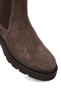 Botín de ante marrón hasta el tobillo con paneles elásticos, puntera redonda y suela de goma texturizada. Detalle de costura a lo largo del borde de la suela.